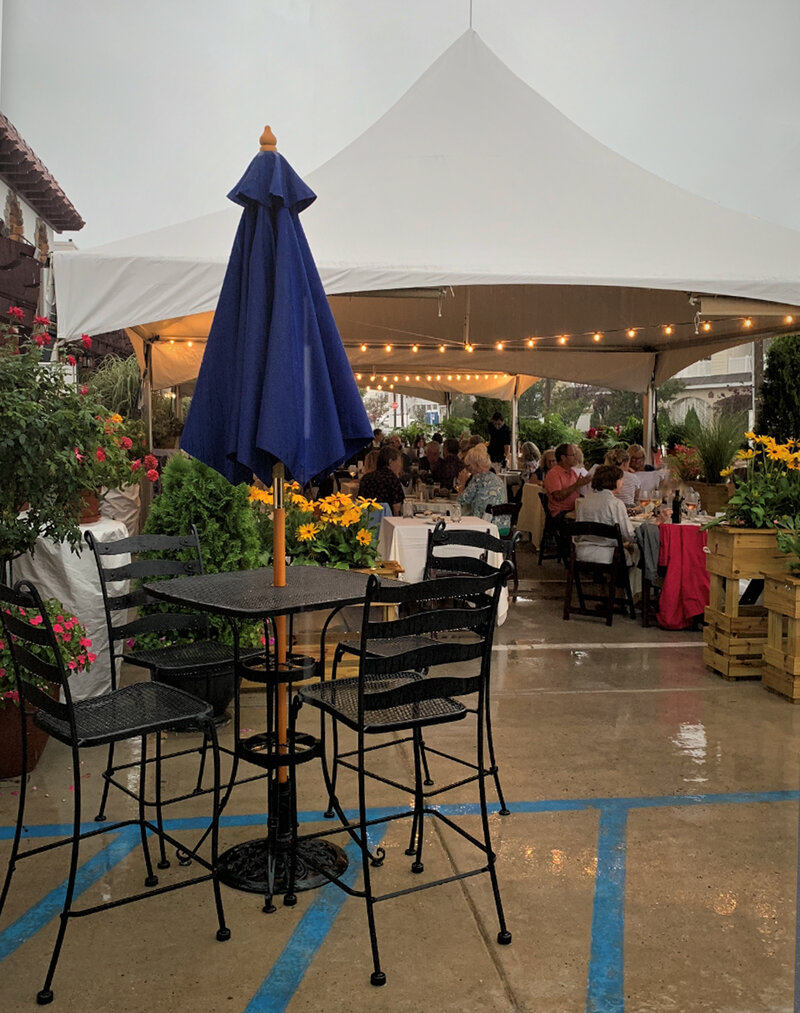 View of peaked tents surrounded with multiple colorful flower beds and guests dining